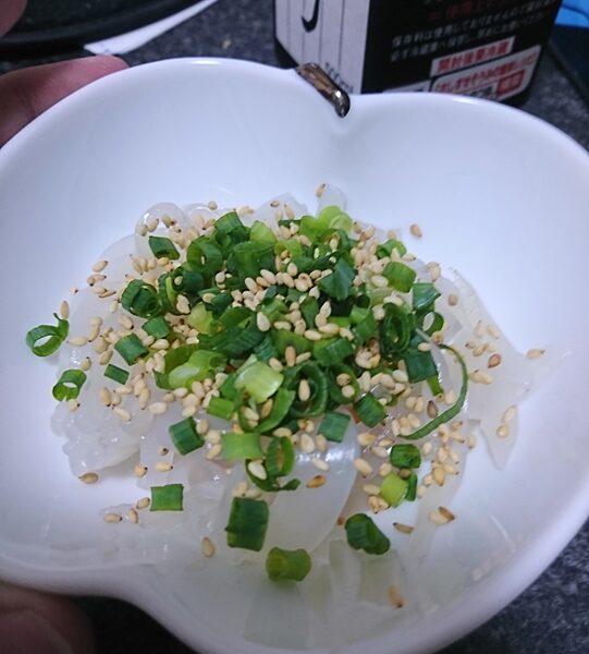 イカそうめん(アオリイカの刺身)に小ネギとゴマがかかっている。創味のつつが見切れている。