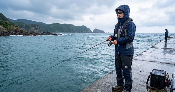 雨の堤防で装備ばっちりで釣りをする女性アングラー