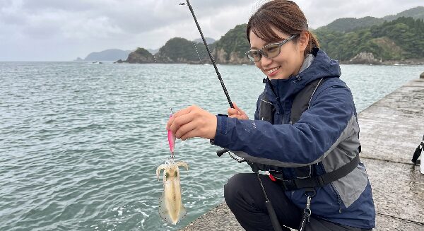 エギにかかった小ぶりなアオリイカを見てほほ笑む女性アングラー