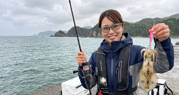 女性アングラーが笑顔で釣れたアオリイカとタックルを持っている